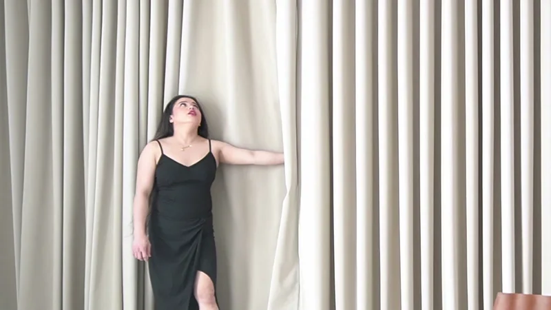 Hermi performing beside floor-length curtains and a bright window